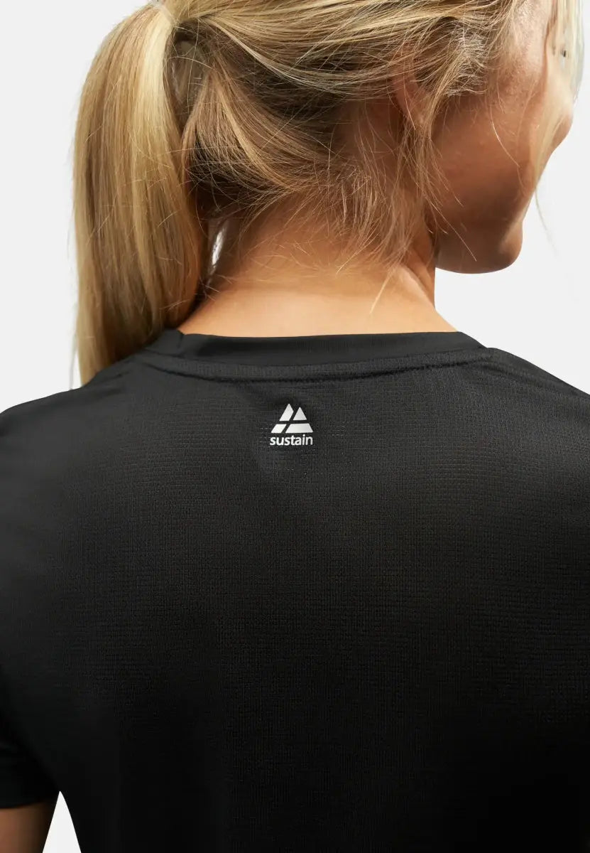 Woman in a black sports T-shirt with "sustain" logo, hair in a ponytail, rear view.