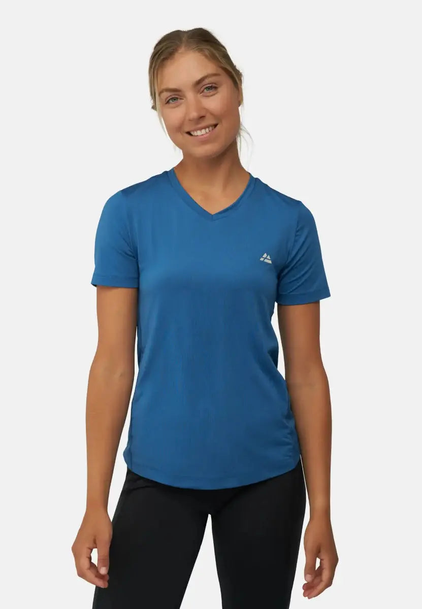 Woman in blue V-neck sports T-shirt with logo, wearing black pants, smiling at camera.