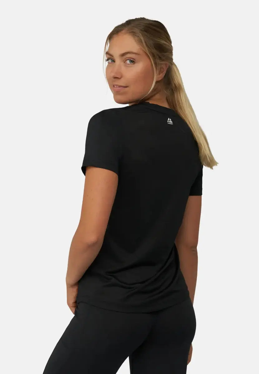 Woman in a black sports t-shirt, facing away, looking over her shoulder, with a subtle smile.