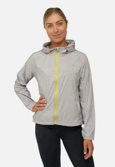 Woman in gray windbreaker jacket with yellow zipper and hood, hands on hips, smiling.