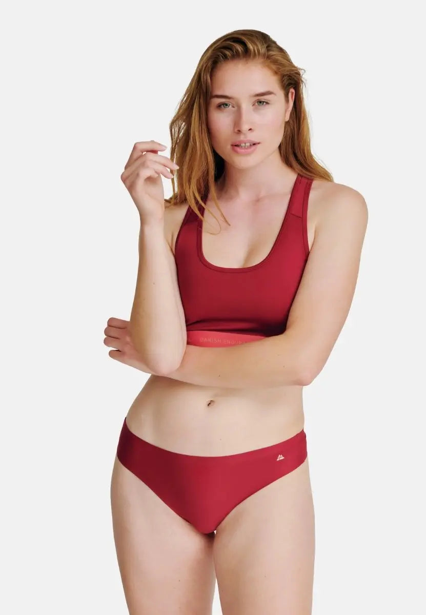 Person wearing red sports bra and thong panties, posing against a plain white background.
