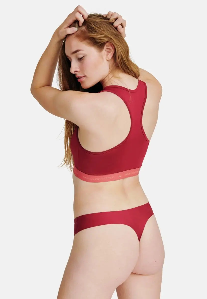 Woman in red sports bra and thong, posing with hand on head, showcasing INVISIBLE THONG PANTIES.