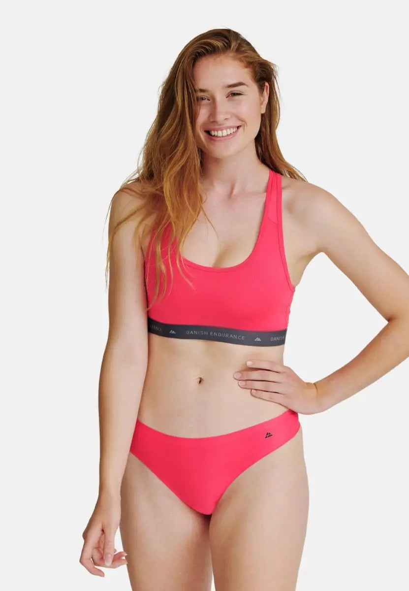 Woman in bright pink sports bra and thong, smiling confidently.