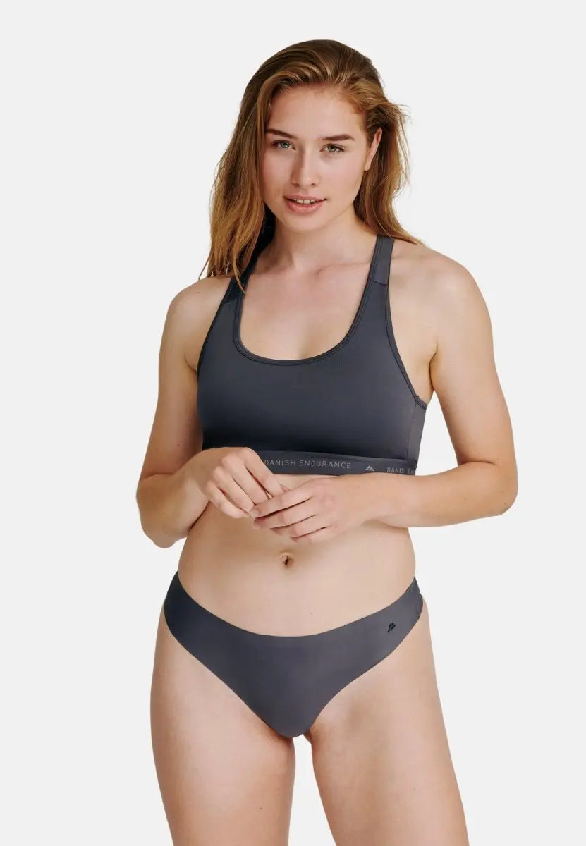 Woman in gray sports bra and thong panties, standing against a plain white background.