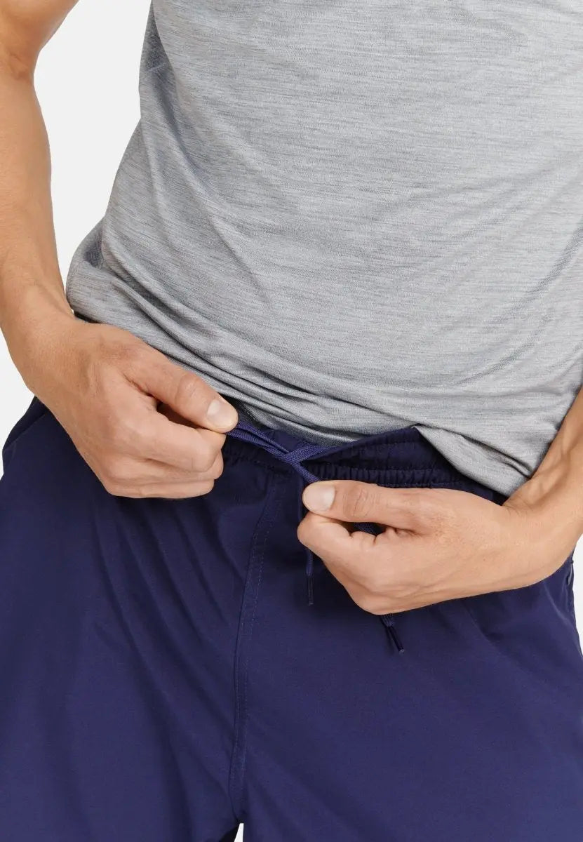 Person tightening drawstring on navy blue sports shorts, wearing a gray shirt.