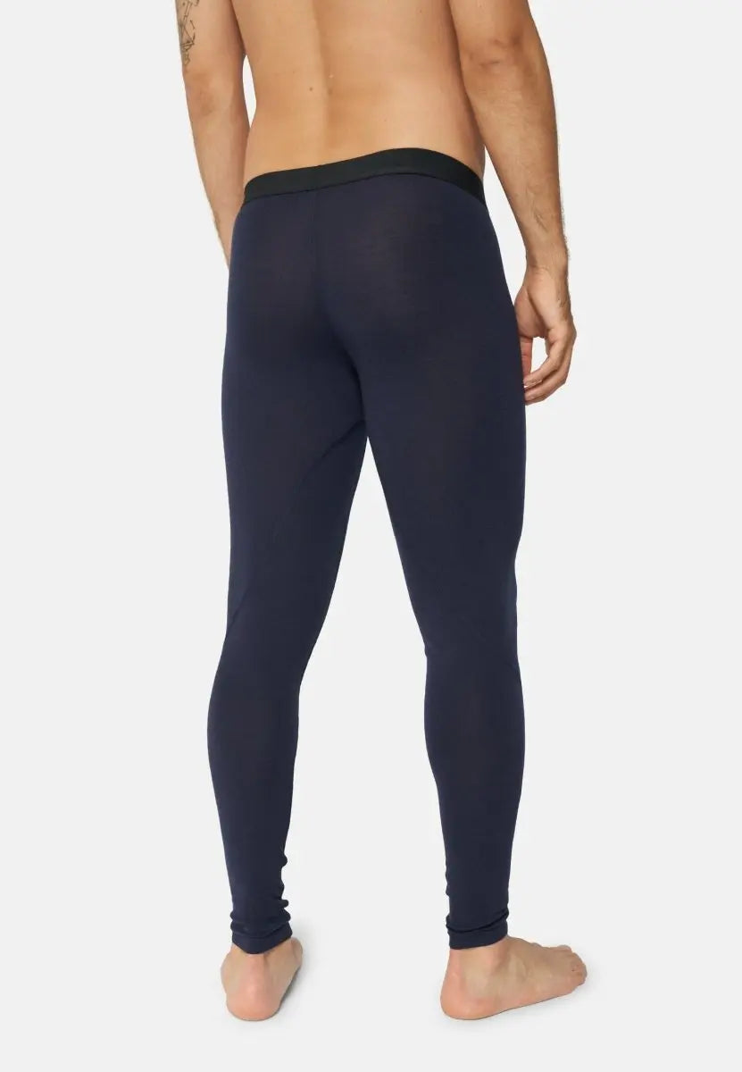 Man from the back in navy merino wool base layer pants, barefoot, white background.