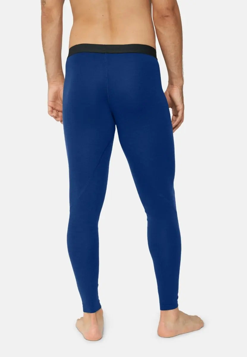 Back view of blue merino wool base layer pants with black waistband, worn by a barefoot man.