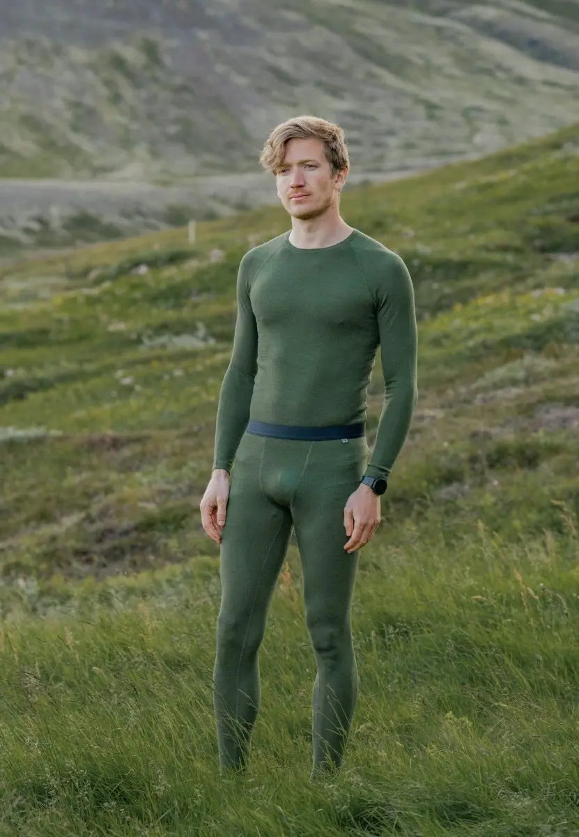 Man wearing green merino wool base layer pants and top, standing in a green field.