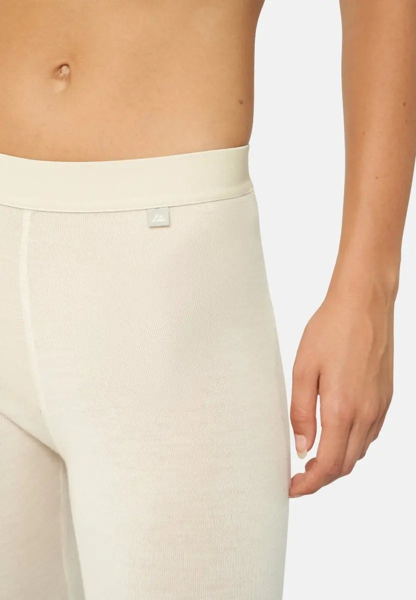 Beige merino wool base layer pants on a woman's torso, showing waistband and fabric texture.