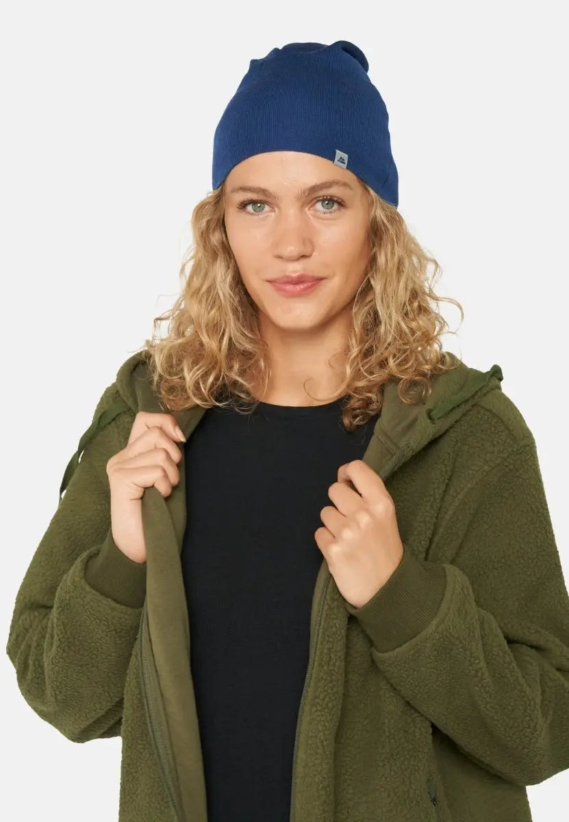 Person wearing a blue beanie with logo, black top, and green jacket, looking at the camera.