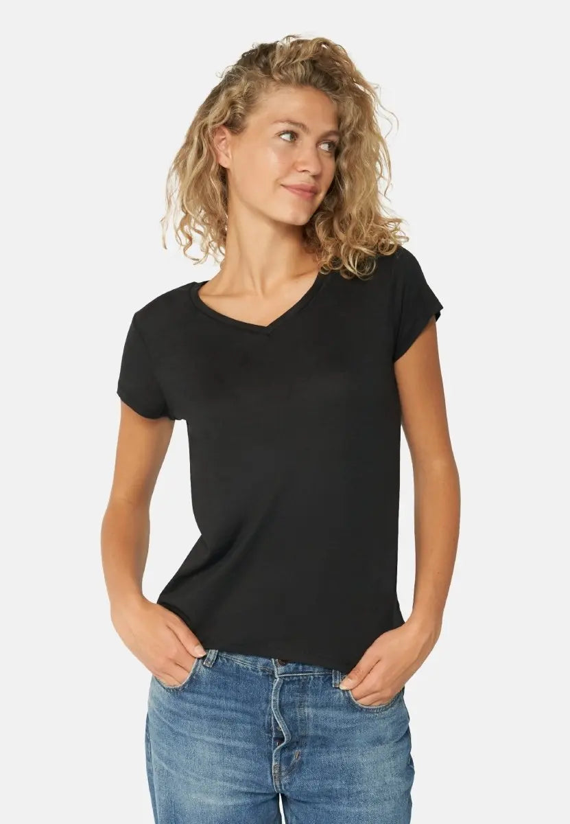 Woman in black V-neck T-shirt and blue jeans, hands in pockets, gazing to the side.