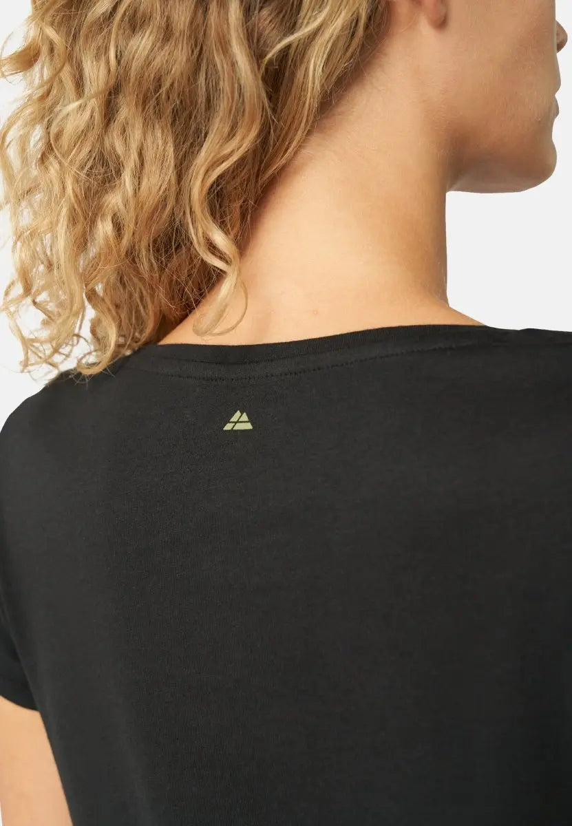 Back view of black V-neck T-shirt with a small logo, worn by a woman with curly blonde hair.