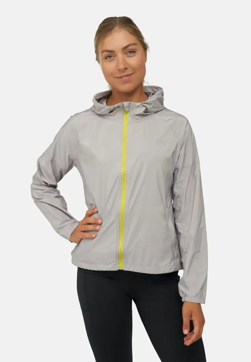 Woman wearing a gray windbreaker with yellow zipper, hand on hip, smiling against a white background.