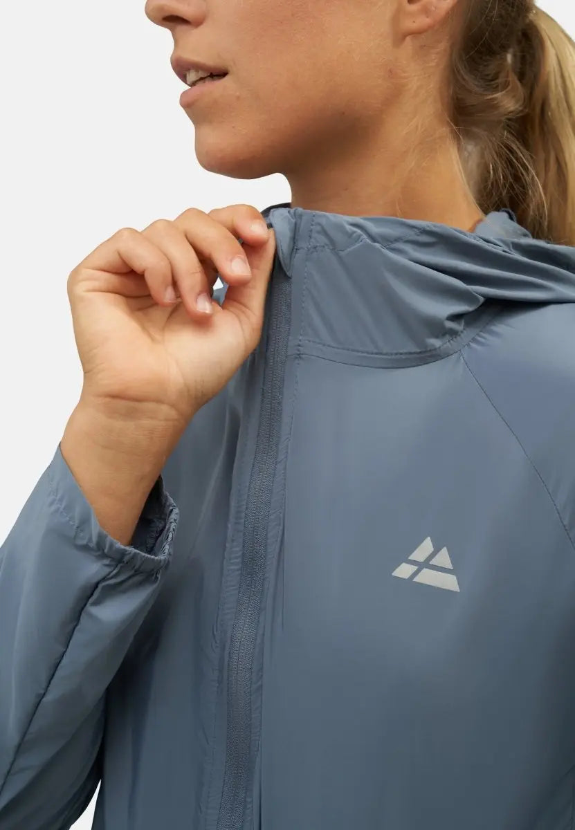 Woman zipping a blue windbreaker jacket with a logo on the chest, showing a close-up of the design.