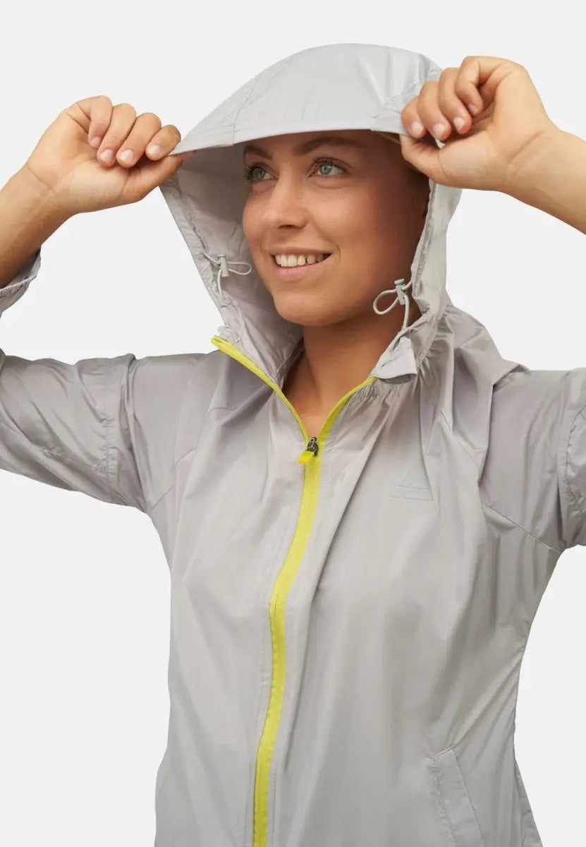 Woman in a light gray windbreaker with a yellow zipper, adjusting the hood and smiling.