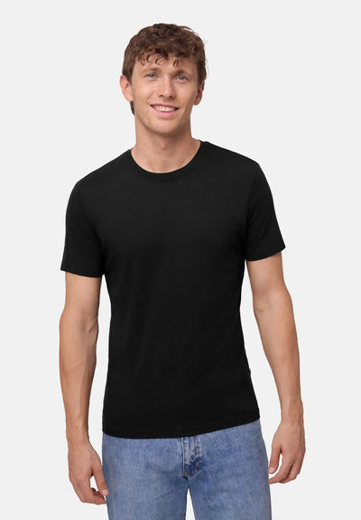 Man wearing a black merino T-shirt and blue jeans, smiling against a plain background.
