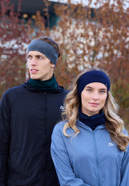 Two people wearing merino headbands, one gray, one navy, standing outside with autumn foliage.